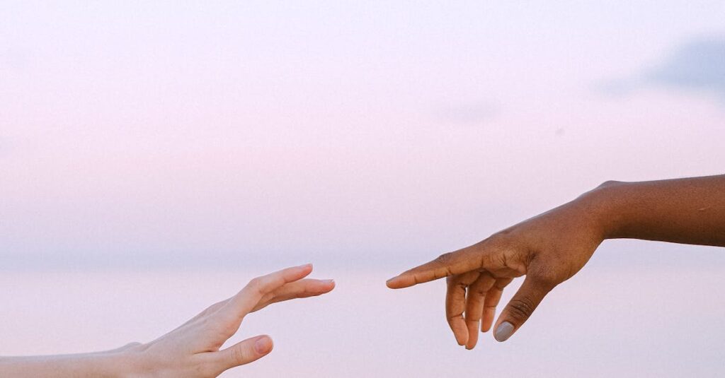 Two diverse hands reaching towards each other over a serene pastel sky and water background.